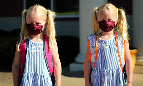 Two girls smile while wearing masks